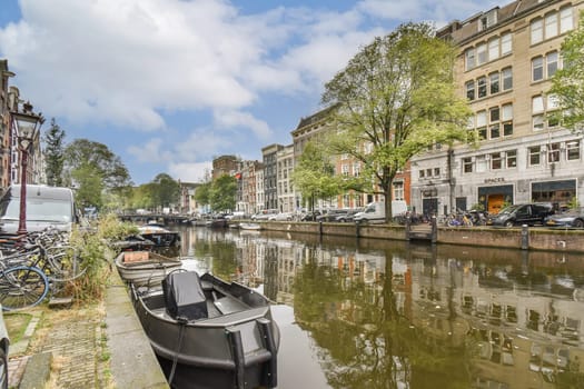 A picturesque view of a canal in Amsterdam surrounded by lush trees, lined with bicycles, showcasing the vibrant city life and architectural beauty.