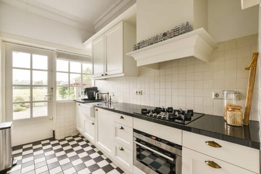 A stylish kitchen combines modern appliances and classic cabinetry, featuring a checkerboard floor and ample natural light from large windows.