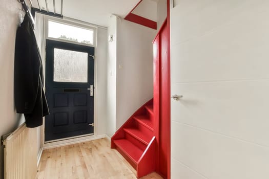 This entrance hall features a stylish design with a bold red staircase and a classic blue front door, combining modern aesthetics with functional space.