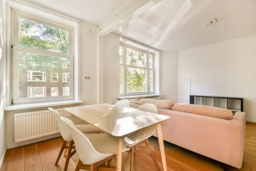 This spacious and stylish living room features a pink sofa, a wooden dining table, and large windows allowing plenty of natural light, providing a serene atmosphere.