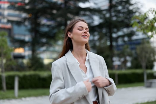 A joyful woman dressed in a stylish blazer and blouse, exuding confidence in a green urban park surrounded by contemporary architecture, perfect for business-themed imagery.