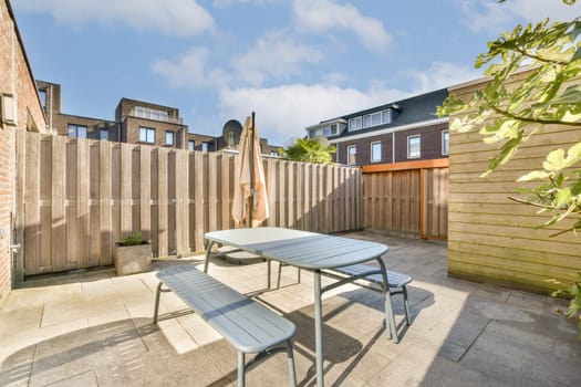 A bright and inviting outdoor patio featuring a table and bench set against a wooden fence, perfect for relaxation and dining in the sun.