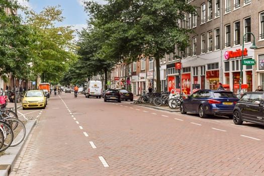 A vibrant city street showcasing parked bicycles, cars, and shops, adorned with trees lining the avenue, reflecting daily urban life.