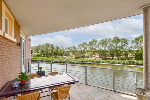 A modern balcony overlooking a serene river, framed by lush greenery and blue skies, creating a tranquil and inviting atmosphere for relaxation.