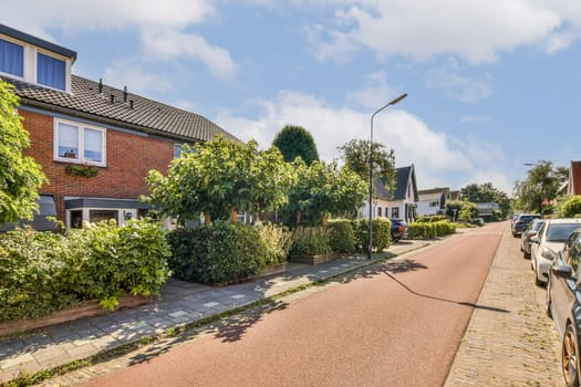 A picturesque view of a quiet residential street lined with trees and neatly trimmed hedges. The sunny sky complements the serene environment.