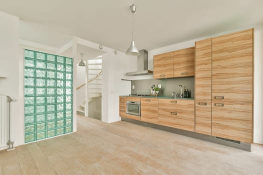 A stylish modern kitchen featuring wooden cabinets, sleek appliances, and unique green glass brick wall. The open layout enhances functionality and aesthetics.