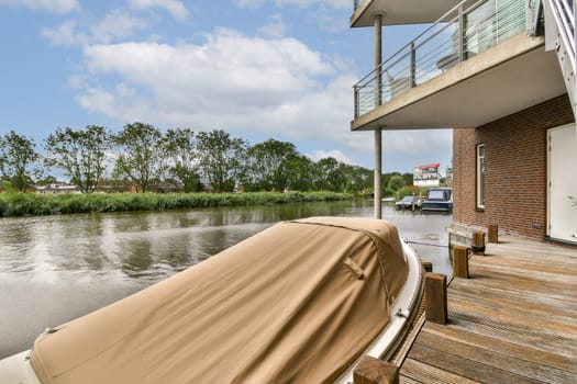 A tranquil view of a waterfront area featuring a moored boat along the bank, surrounded by lush greenery and modern architecture in the background.
