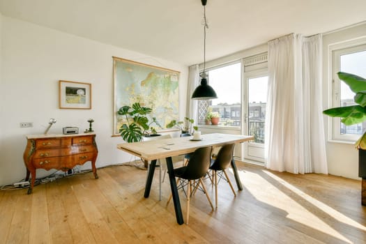 A stylish dining space featuring a wooden table, black chairs, and large windows. The room is decorated with a world map and indoor plants, showcasing modern design.