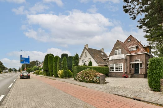 A serene roadside scene featuring charming houses surrounded by lush greenery and well-maintained hedges, providing a picturesque urban landscape.