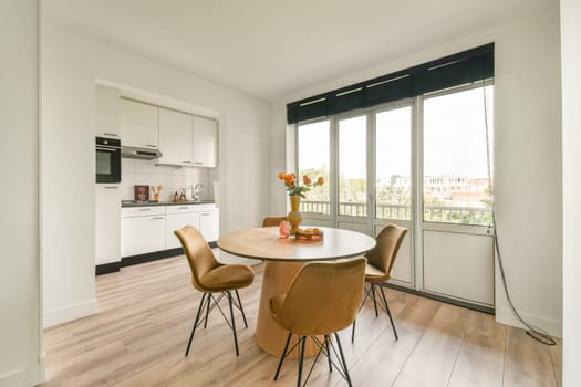 A contemporary dining area featuring a round table, chairs, and large windows that offer abundant natural light, creating a warm atmosphere.