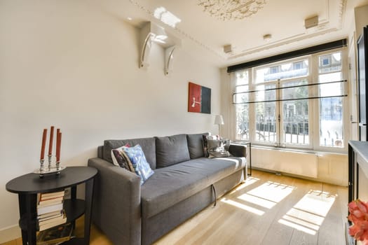 A stylish living room featuring a comfortable sofa, tasteful artwork, large windows, and natural light. The space combines modern design with cozy elements.