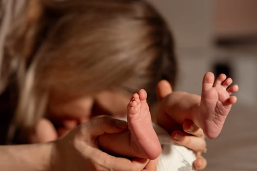 A mother gently holds her babys tiny feet while leaning in for a kiss at home. The warm atmosphere captures their close bond in a loving moment.