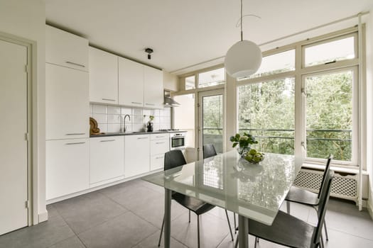 A contemporary kitchen featuring sleek cabinetry, a glass dining table, and large windows that provide ample natural light, creating an inviting atmosphere.