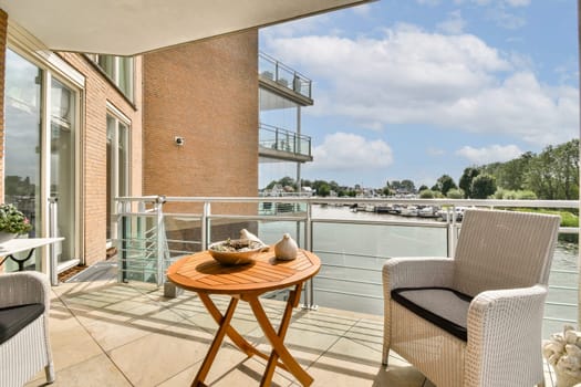 A beautifully designed balcony featuring a round table, two chairs, and a stunning view of water and greenery. Perfect for relaxation and enjoying nature.