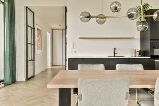 A sleek and contemporary kitchen featuring a stylish dining area with a wooden table, elegant lighting fixtures, and a modern aesthetic.