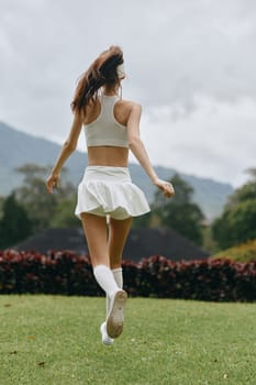 Fit woman in white athletic outfit enjoys jogging in a lush green landscape, representing a healthy lifestyle and outdoor fitness