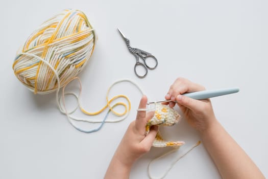 Child crocheting with colorful yarn on white background.
