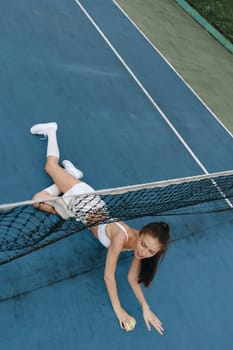 An athletic young woman in sporty wear shows her dedication to tennis while attempting to catch a ball on a vivid blue court, embodying empowerment and sportiness