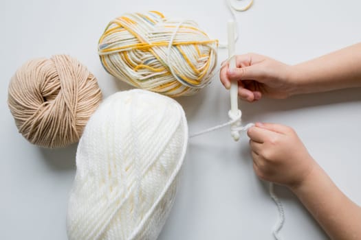 Child crocheting with white yarn and multicolored wool balls.