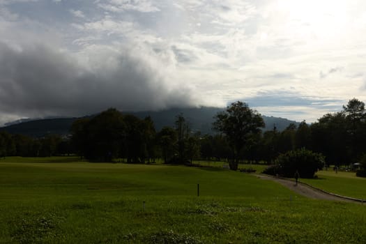 A stunning view of a golf course featuring a vibrant green landscape, dotted with trees and hills under a dramatic cloudy sky Perfect for golf enthusiasts