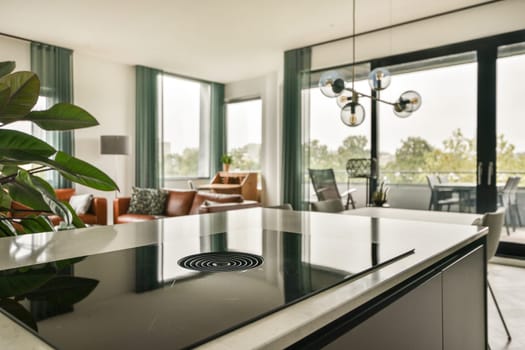 A stylish modern kitchen featuring sleek furnishings, large windows, and greenery, creating a bright, inviting atmosphere for cooking and entertaining.