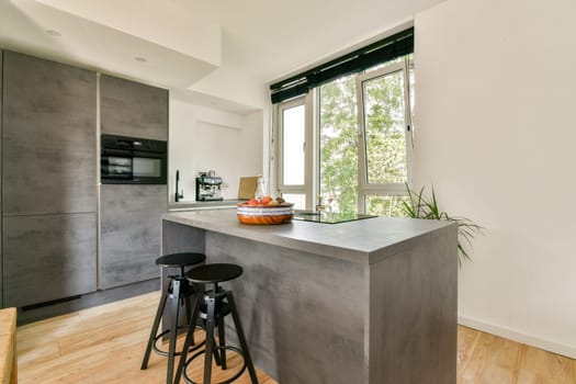 A sleek modern kitchen featuring a gray island with stools, natural light from large windows, and minimalist decor, creating an inviting cooking space.