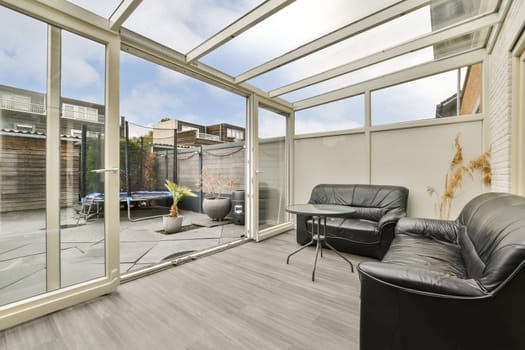 A modern indoor patio showcasing large glass panels, sleek furniture, and a serene outdoor view. Ideal for relaxation and enjoying nature indoors.