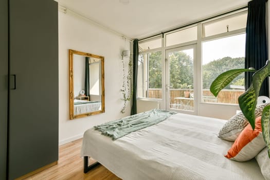 A sleek and modern bedroom design featuring large windows, natural light, and stylish decor elements such as a mirror and plants, creating a serene atmosphere.
