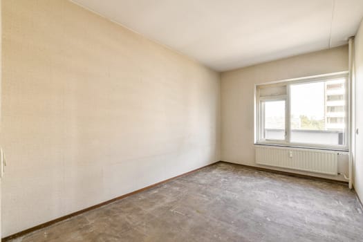 A vacant room featuring a large window that allows natural light to brighten the space, highlighting the simple walls and floor in a minimalistic design.