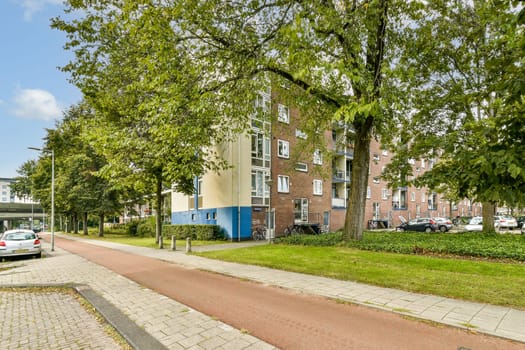 A scenic view of a residential street lined with trees, showcasing modern apartment buildings and parked cars. A calm atmosphere in an urban setting.