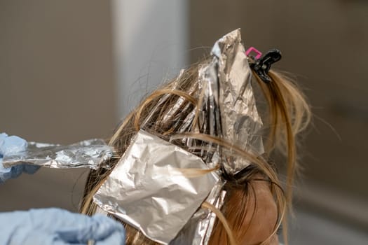 A person is getting their hair colored with foils applied to sections for highlighting. The hairdresser is actively working on the hair.