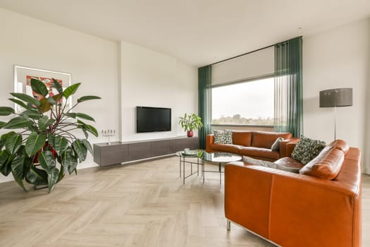 A stylish modern living room featuring a brown leather sofa, large windows with natural light, and decorative plants, creating a cozy and inviting atmosphere.