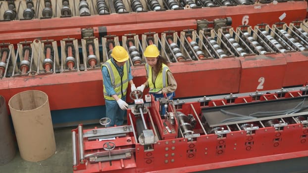 Engineer and operator wearing a safety suit maintaining machine in industrial metal sheet factory, team worker walk teaching help friend operate control heavy machine in factory with many equipment