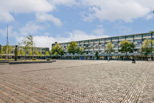 A spacious urban plaza featuring modern buildings and lush greenery, bustling with people and surrounded by clear blue skies, showcasing contemporary city life.