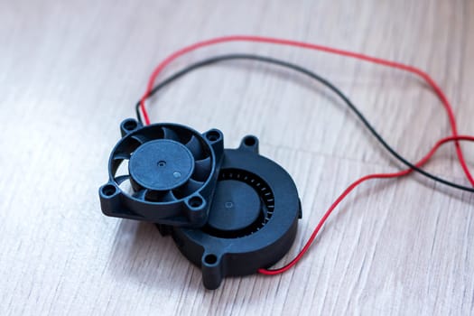 A compact, smallsized black fan that features red wires connected to it for its functioning and operation purposes