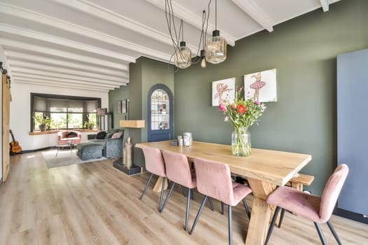 A modern dining space featuring a wooden table, elegant pink chairs, and a beautiful floral centerpiece, surrounded by a contemporary interior design.