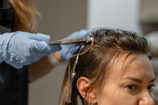 A stylist carefully applies hair dye to a clients hair using foil in a contemporary salon environment, showcasing a creative color transformation.
