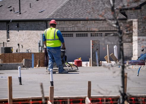A construction worker uses a concrete finishing machine to smooth a fresh concrete slab on a new foundation