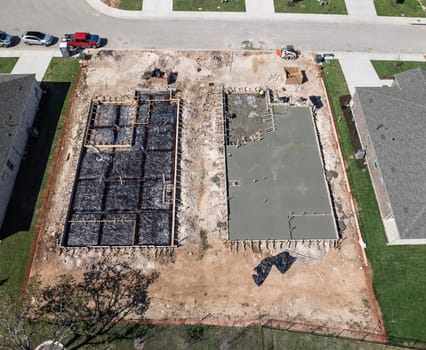Overhead view of two construction sites, one with a concrete slab and the other a framed foundation ready for concrete