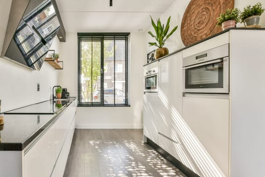 A sleek, modern kitchen featuring minimalistic cabinetry and contemporary appliances, enhanced by natural light filtering through window blinds.