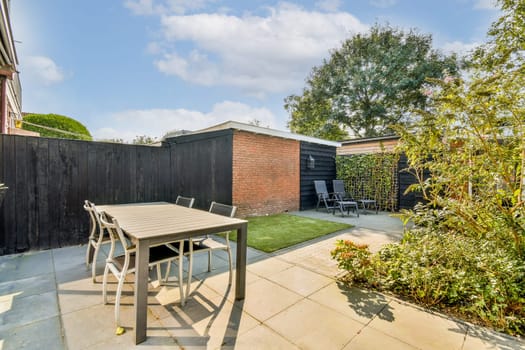 A contemporary outdoor patio featuring a sleek table and chairs surrounded by lush plants, and a clear blue sky in the background.