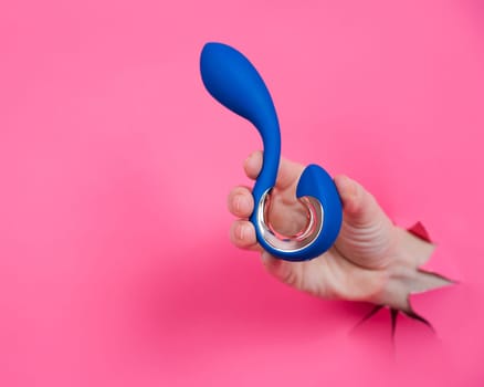 Hand with blue vibrator sticking out through pink paper background