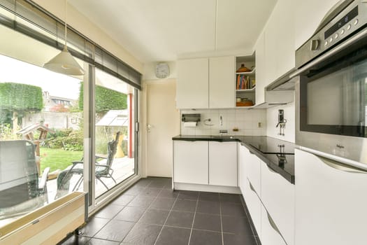 A sleek and modern kitchen featuring white cabinets, dark countertops, and ample natural light from large windows, creating a warm and inviting atmosphere.