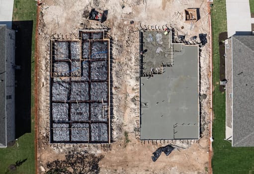 Overhead view of two construction sites, one with a concrete slab and the other a framed foundation ready for concrete