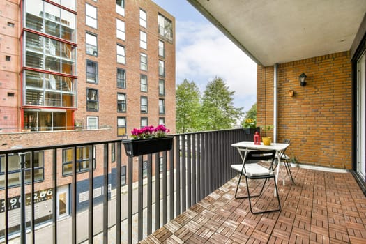 A stylish balcony featuring modern furniture and a beautiful plant display, overlooking an urban landscape with vibrant buildings and clear skies.