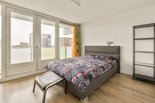 A contemporary bedroom featuring a floral-patterned bedspread, a minimalist design, and large windows leading to a balcony. A serene and stylish environment.