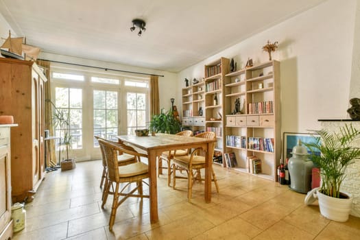 A charming dining space features a wooden table, shelves filled with books, and an abundance of natural light pouring through large windows.