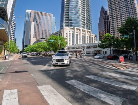 Austin, TX - 10 April 2025: Fisheye lens view of a Waymo Jaguar autonomous taxi turning at junction in downtown Austin, Texas