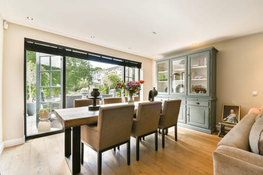 A stylish living room featuring a modern dining area, large windows, and tasteful furniture. The design emphasizes comfort and contemporary aesthetics.