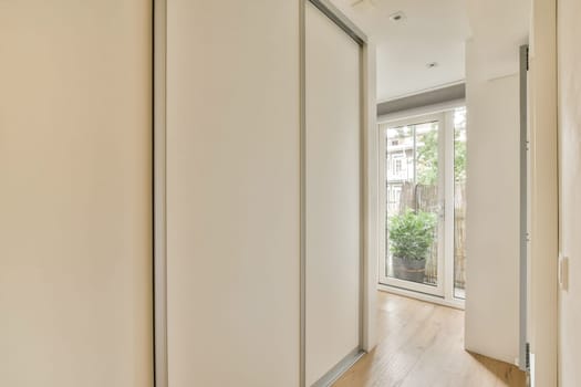 A stylish interior hallway featuring sleek white walls, wooden flooring, and large windows allowing natural light to fill the space.